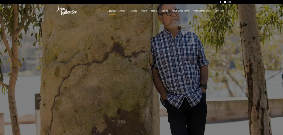 John Williamson website home page: John Williamson leaning against a gum tree, under the site navigation